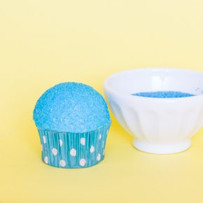 Covering a cupcake in sprinkles to make a snow cone cupcake.