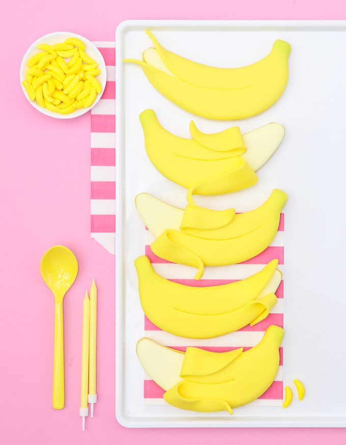 five banana cookies with yellow banana candies on pink backdrop