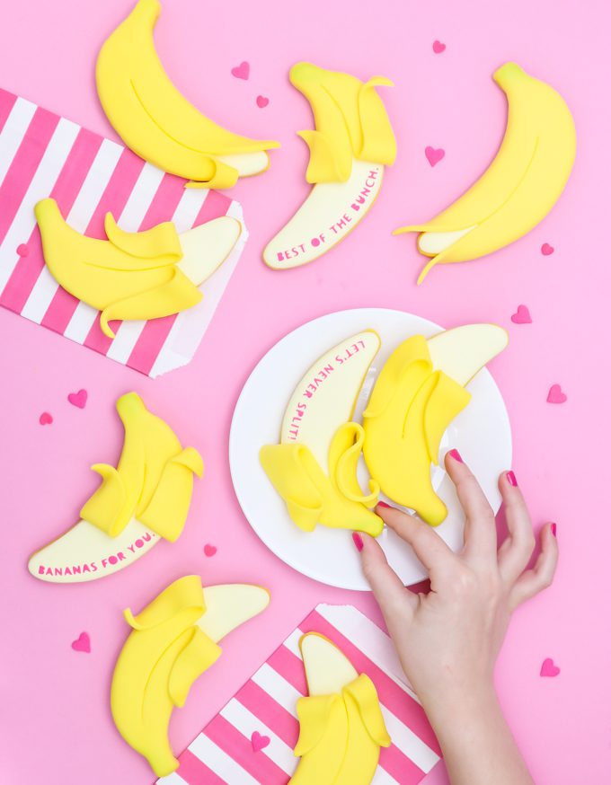 many banana cookies on pink backdrop with a hand peeling one