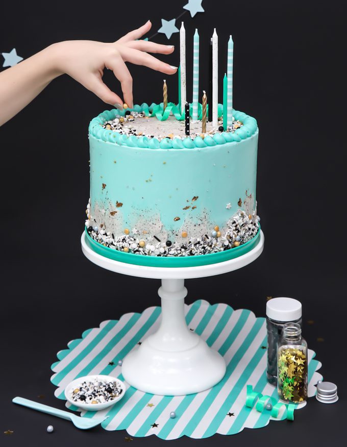 mint blue cookies and cream cake on stand with a hand over top