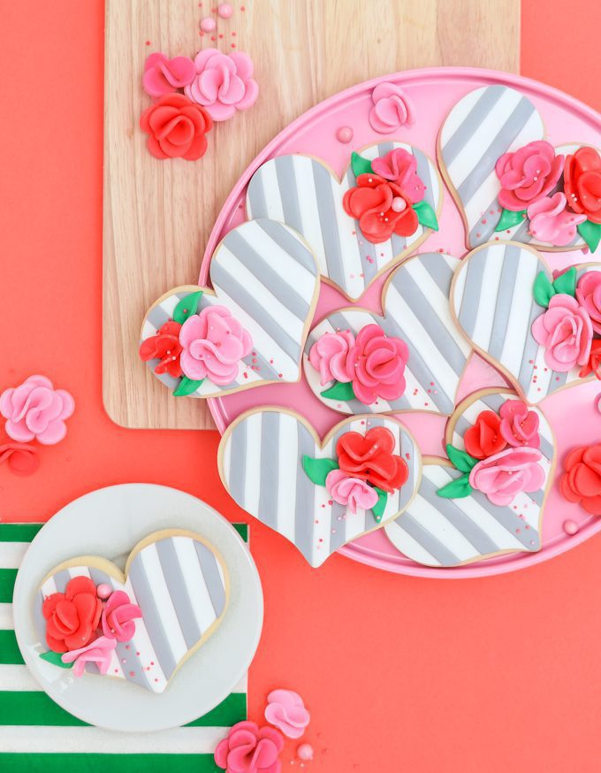 Pink platter of grey and white striped fondant cookies with flowers on top.