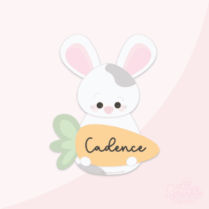 Clipart of a white bunny with grey spots holding an orange carrot with the name Cadence on it in cursive black text.