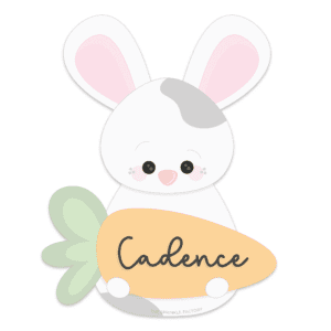 Clipart of a white bunny with grey spots holding an orange carrot with the name Cadence on it in cursive black text.